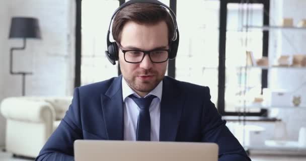 Male executive wears headset video calling by webcam on laptop — Stock Video