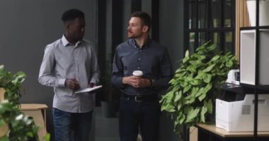 Afrika kökenli Amerikalı genç bir çalışan Kafkasyalı bir yöneticiyle ofiste yürüyor..