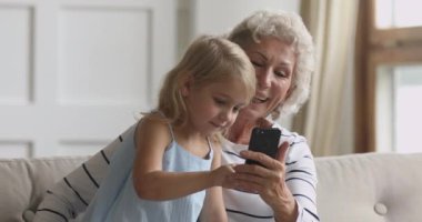 Küçük kız, yaşlı büyükannesiyle cep telefonu kullanıyor..