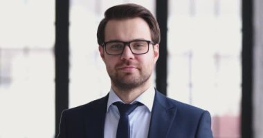 Takım elbiseli ve gözlüklü güler yüzlü işadamı kameraya bakıyor.