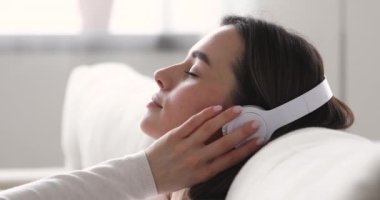 Huzurlu genç bayan, kanepede dinleniyor, kulaklık takıyor, müzik dinliyor.