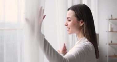 Mutlu genç bir kadın pencereyi açar. Pencere kenarına bakar.