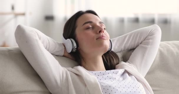 Klidná uvolněná mladá žena chlazení na gauči nošení sluchátek — Stock video