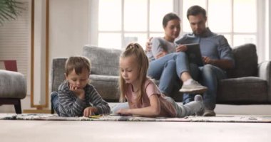 Ebeveynler dijital tablet kullanırken küçük çocuklar resim çiziyor.