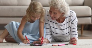 Evde olgun bir büyükanneyle çizim yapan mutlu küçük kız..