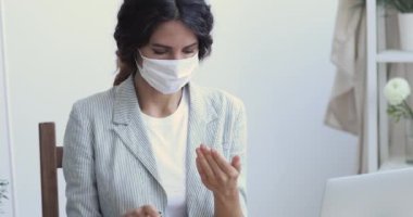 Kadın ofis çalışanı maske takıyor dezenfektanla elleri dezenfekte ediyor.