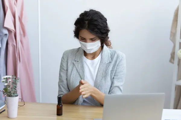 Woman in facemask cleans hands using sanitizer spray at workplace — Stock Photo, Image