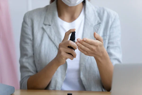 Woman in mask cleans hands using sanitizer spray — Stock Photo, Image
