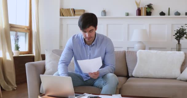 Молодой человек проверяет счета на оплату онлайн на дому — стоковое видео
