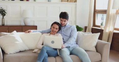 Kanepede dizüstü bilgisayar kullanarak gülümseyen genç bir çift.