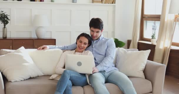 Sonriente pareja de jóvenes adultos utilizando el ordenador portátil en casa en el sofá — Vídeo de stock