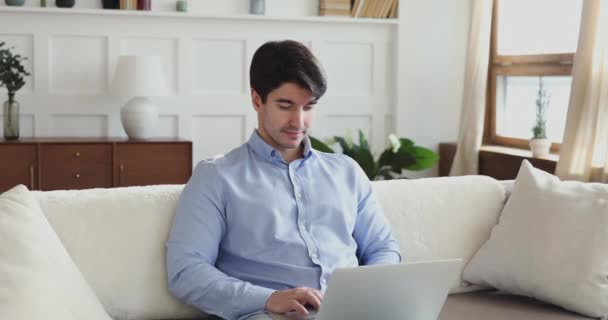Millennial człowiek za pomocą laptopa siedzi na kanapie w salonie — Wideo stockowe