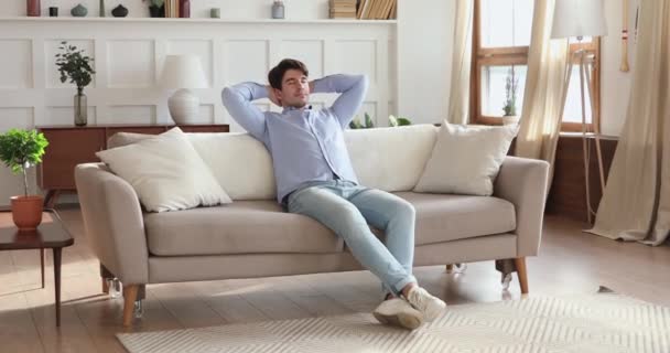 Uomo sorridente che si rilassa in un accogliente soggiorno su un comodo divano — Video Stock