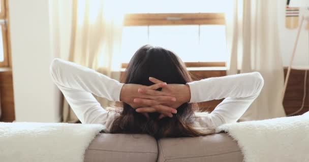 Спокойная привлекательная девушка, опирающаяся на удобный диван, дыша свежим воздухом — стоковое видео