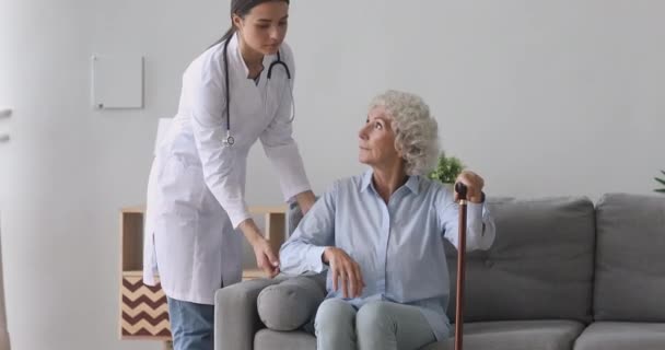 Caring young nurse in uniform helping old disabled hoary woman. — Stock Video