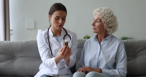 Médico segurando pílulas garrafa, lendo efeitos colaterais para a mulher idosa . — Vídeo de Stock