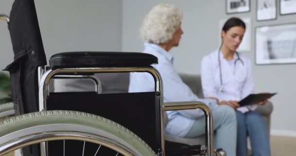 Enfoque en silla de ruedas, consulta con el médico paciente en segundo plano . — Vídeo de stock