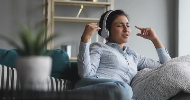 Glad ung indian flicka som ligger på soffan, lyssnar på musik. — Stockvideo