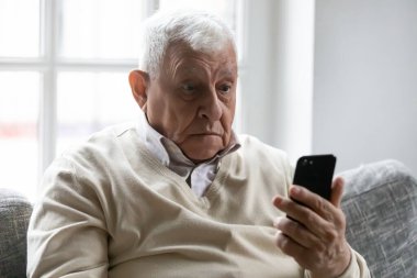 Akıllı telefon tutan yaşlı adam, ekrandaki cihaza bak. Şaşırdı.