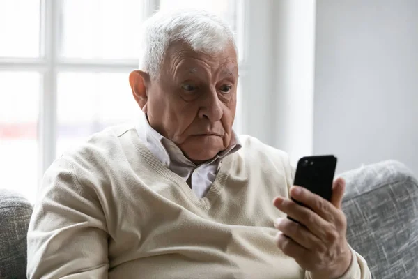 Homem velho segurando olhar smartphone na tela do dispositivo se sente surpreso — Fotografia de Stock