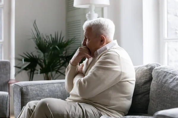 Viejo solitario sentado en un sofá perdido en pensamientos pesimistas — Foto de Stock