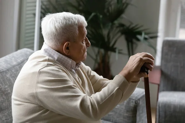 Old man sit on couch holding walking stick feels lonely