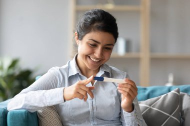 Gülümseyen genç Hintli kadın hamilelik testine bakıyor.