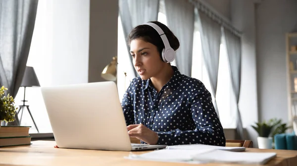 Ocupado jovem indiana mulher vestindo fones de ouvido trabalhando no laptop — Fotografia de Stock