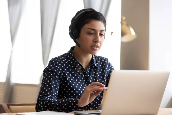 Serious Indian woman wearing headphones talking, using laptop — Stock Photo, Image