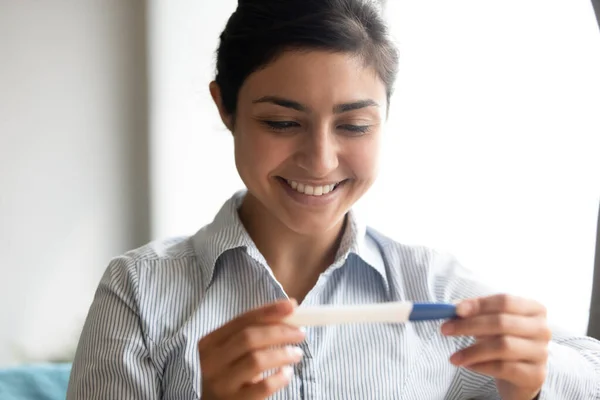 Nær smilende indisk kvinne som ser på graviditetstest – stockfoto