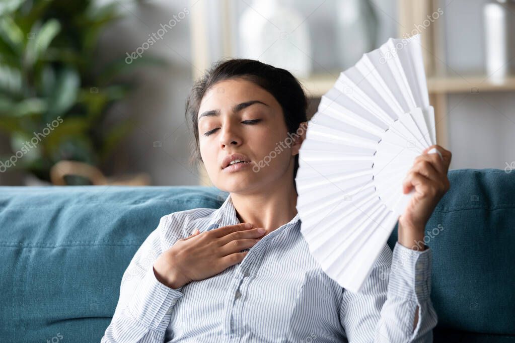 Overheated Indian woman waving paper fan, feeling unwell