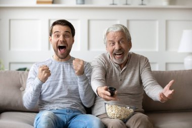 Yaşlı baba ve yetişkin oğul futbol maçı izliyorlar.