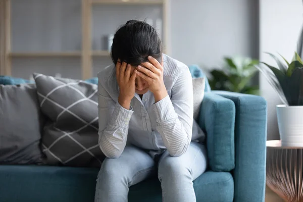 Unhappy depressed Indian woman holding head in hands, sitting alone