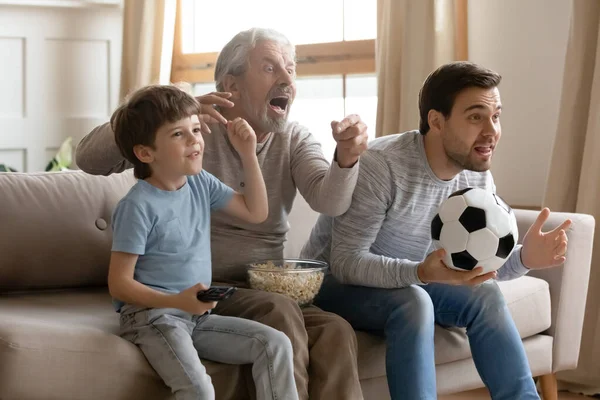 Três gerações de homens assistem jogo de futebol em casa — Fotografia de Stock