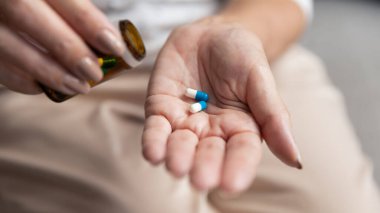 Şişeden ilaç kapsüllerini çıkaran olgun bir kadın..