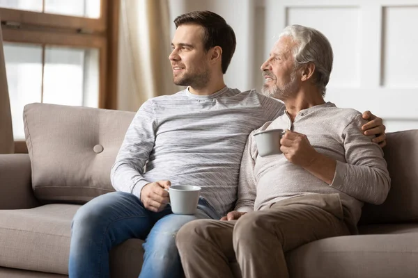 Dreamy senior dad and adult son look in distance visualizing — Stock Photo, Image