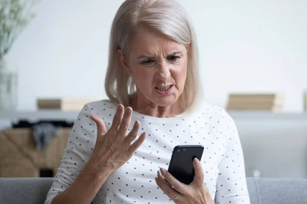 Unhappy middle aged lady irritated by bad smartphone work.