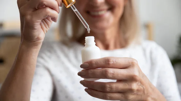 Close up happy older woman opening bottle with essence. — Stock Photo, Image