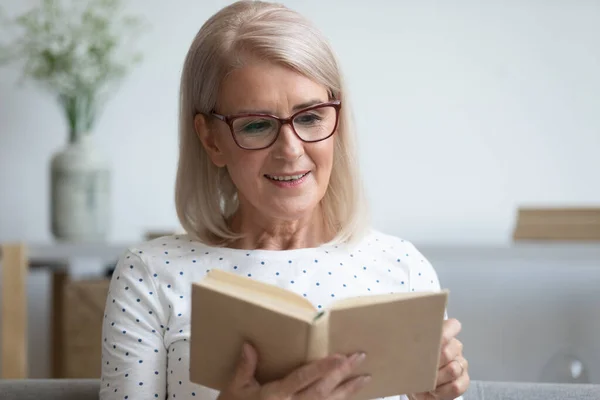 Pleasant middle aged woman in eyeglasses involved in reading book. — Stock Photo, Image