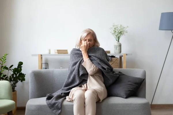 Unhealthy middle aged woman covered in blanket sitting on sofa. — Stock Photo, Image