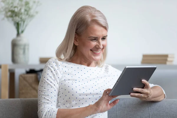 Happy older lady holding computer tablet in hands.