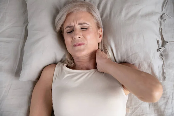 Older unhappy woman lying in bed, feeling strong neck ache. — Stock Photo, Image