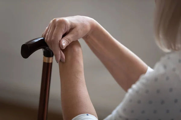 Older retired woman holding hands on wooden cane, close up. — Stock Photo, Image