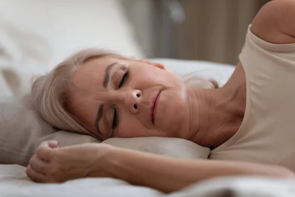 Serene older woman sleeping on comfortable pillow in bedroom.