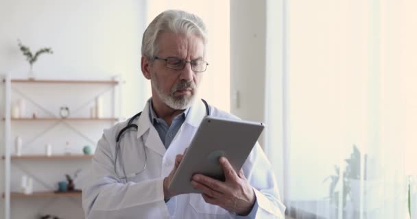Médico adulto mayor serio que usa tableta digital en el trabajo — Vídeo de stock