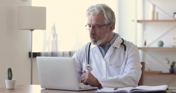 Старший врач разговаривает с пациентом, делая видеозвонок на ноутбуке — стоковое видео