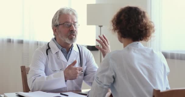 Улыбающийся старый врач-мужчина консультирует пациента, пожимающего руку молодой женщине — стоковое видео