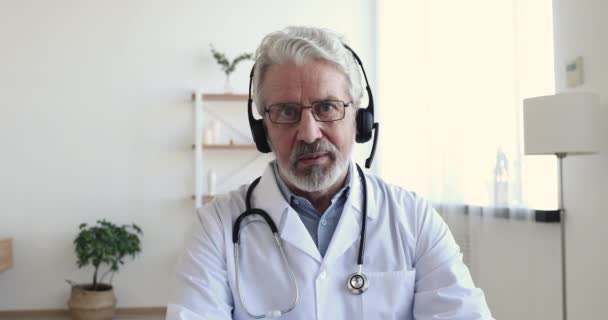 Старший врач носит наушники делает удаленный видеозвонок, просмотр веб-камеры — стоковое видео