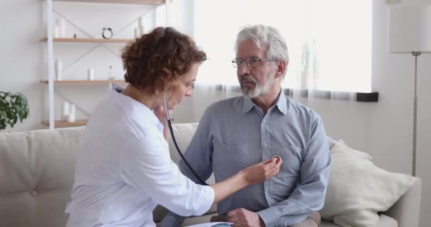 Женщина-врач слушает пожилого пациента со стетоскопом во время домашнего визита — стоковое видео