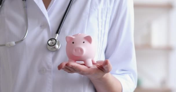 Médica feminina segurando caixa de banco porquinho em mãos, vista close-up — Vídeo de Stock